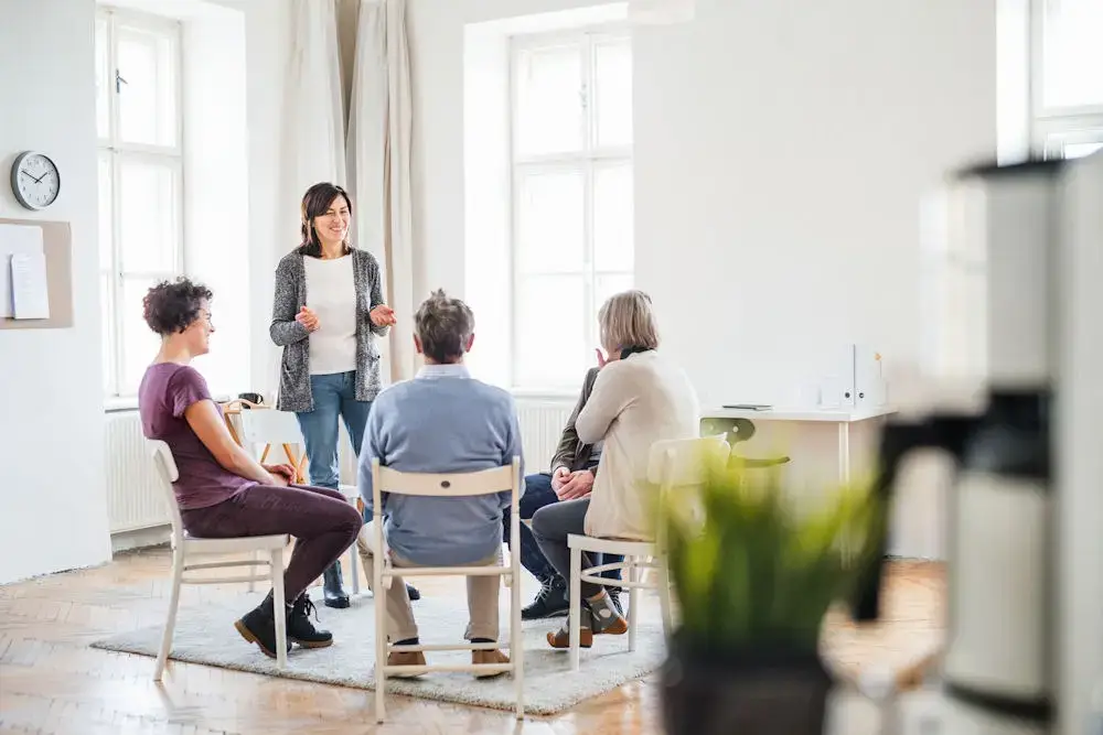 a woman standing while talking to a group of people sitting in circle